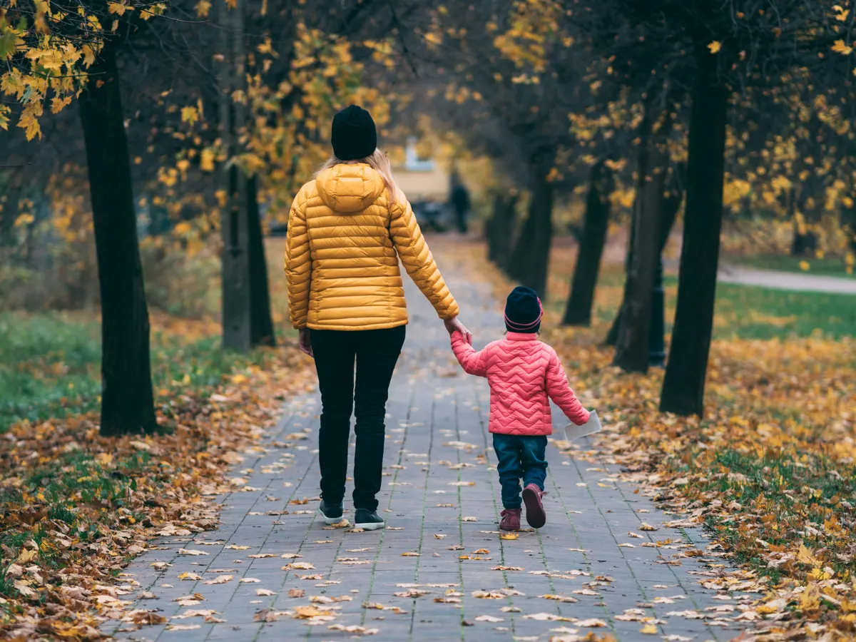 A parent holding a child's hand while walking, seen from behind