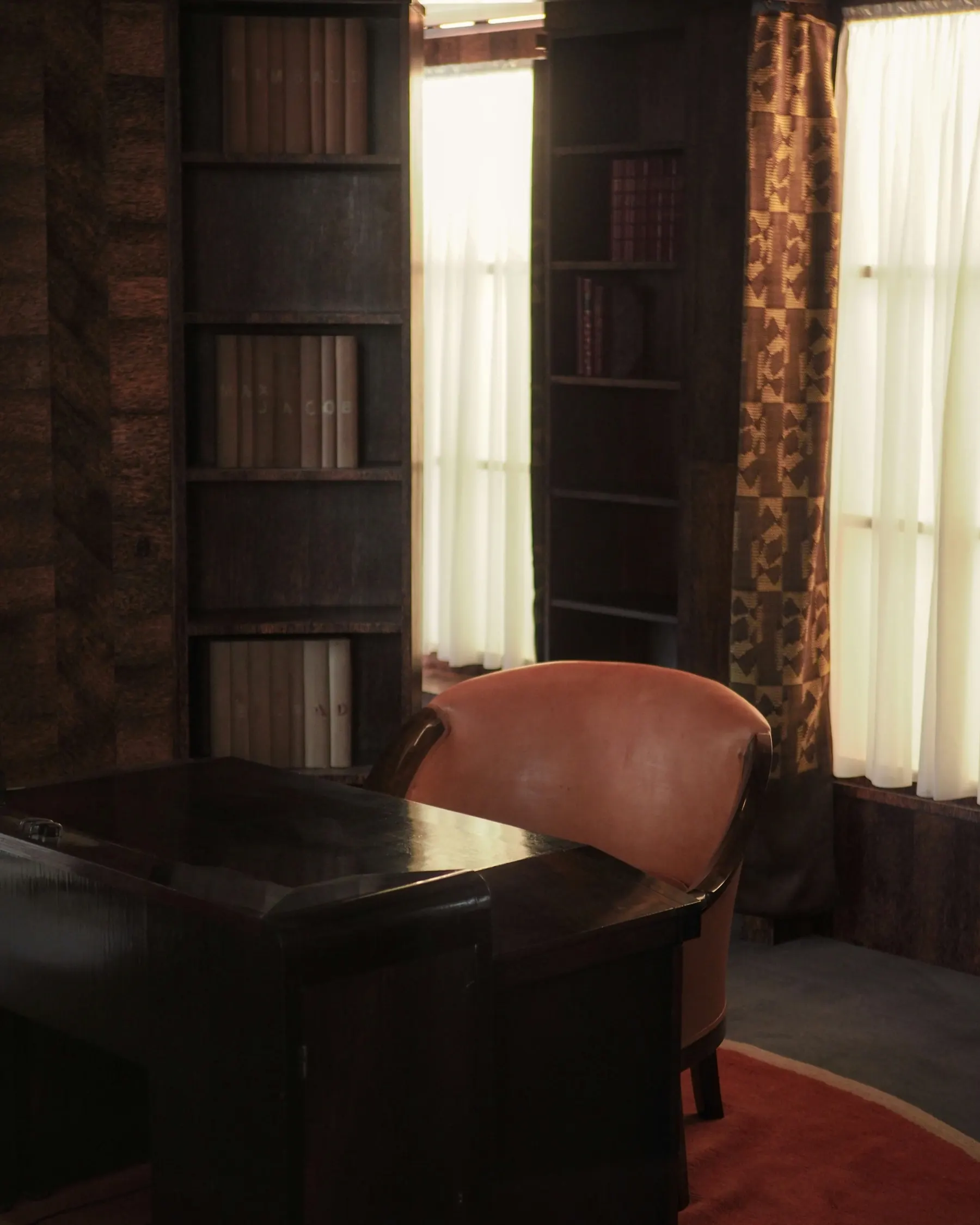 A quiet private office with bookshelves, a leather chair and warm curtained window light
