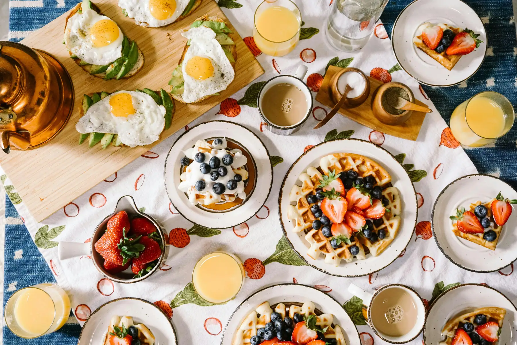 Breakfast spread from above: eggs on avocado toast, waffles with berries, coffee and orange juice