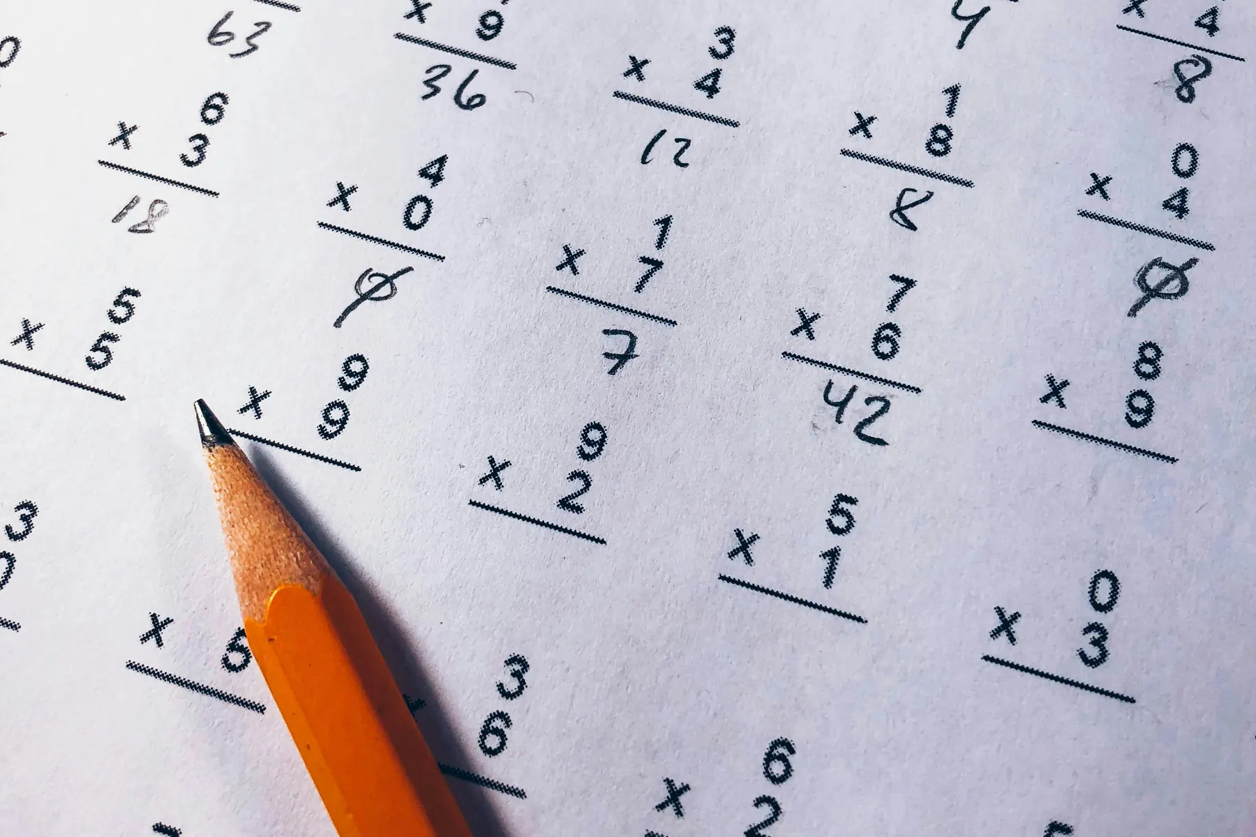 A multiplication worksheet with corrections in pencil, a brown pencil resting on the page