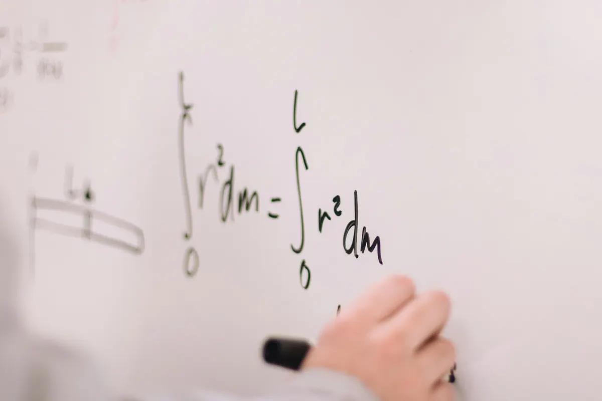 A tutor's hand writing a real math formula on a whiteboard