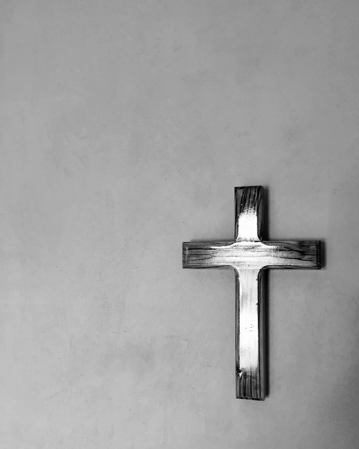 A simple wooden cross mounted on a plain stone-gray wall