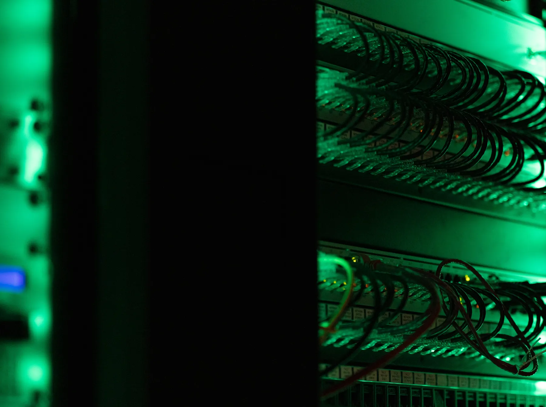 Dark server rack aisle lit by green LED cabling, network switches close up
