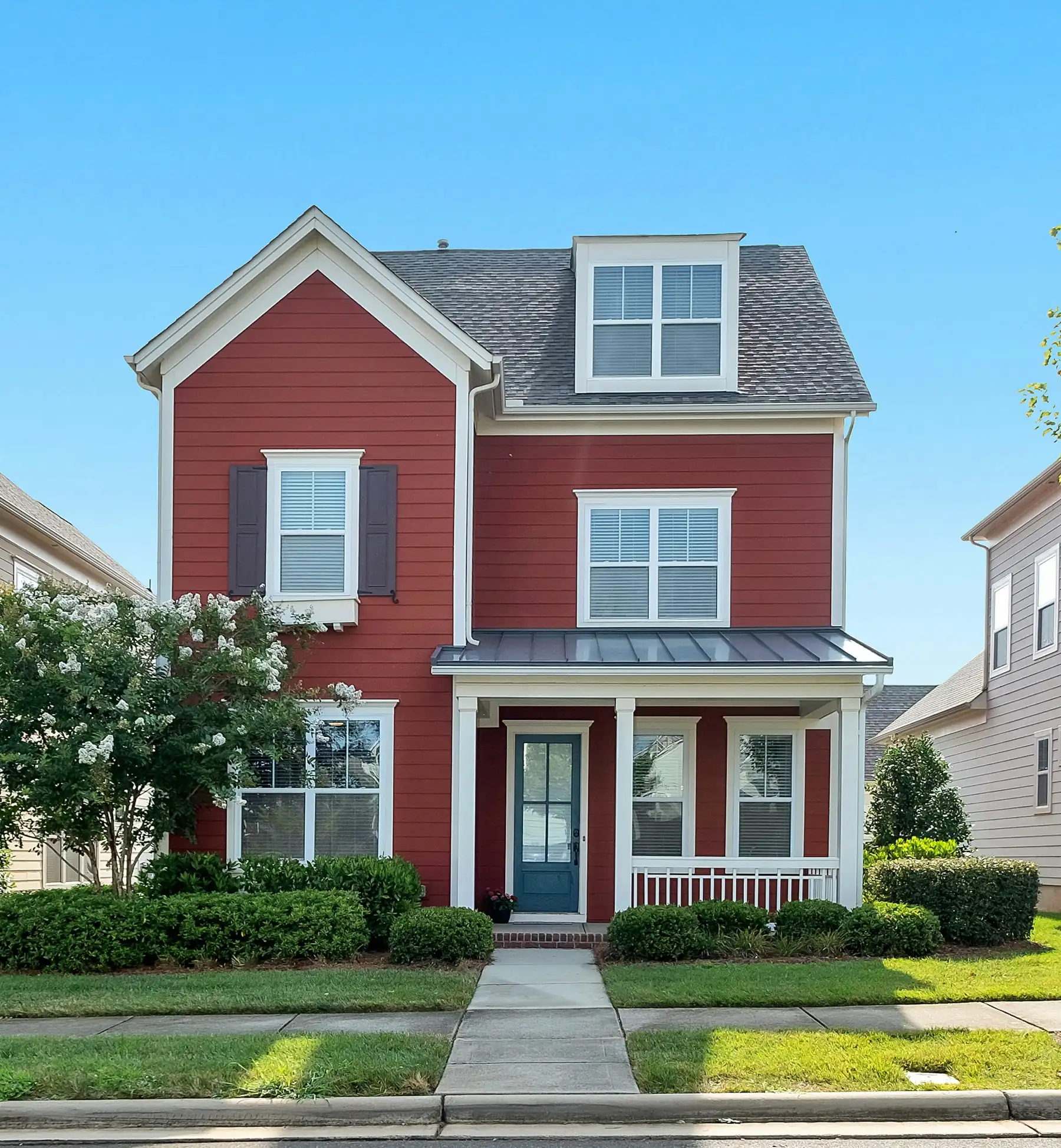 Red two-story house with a white front porch on a tree-lined street