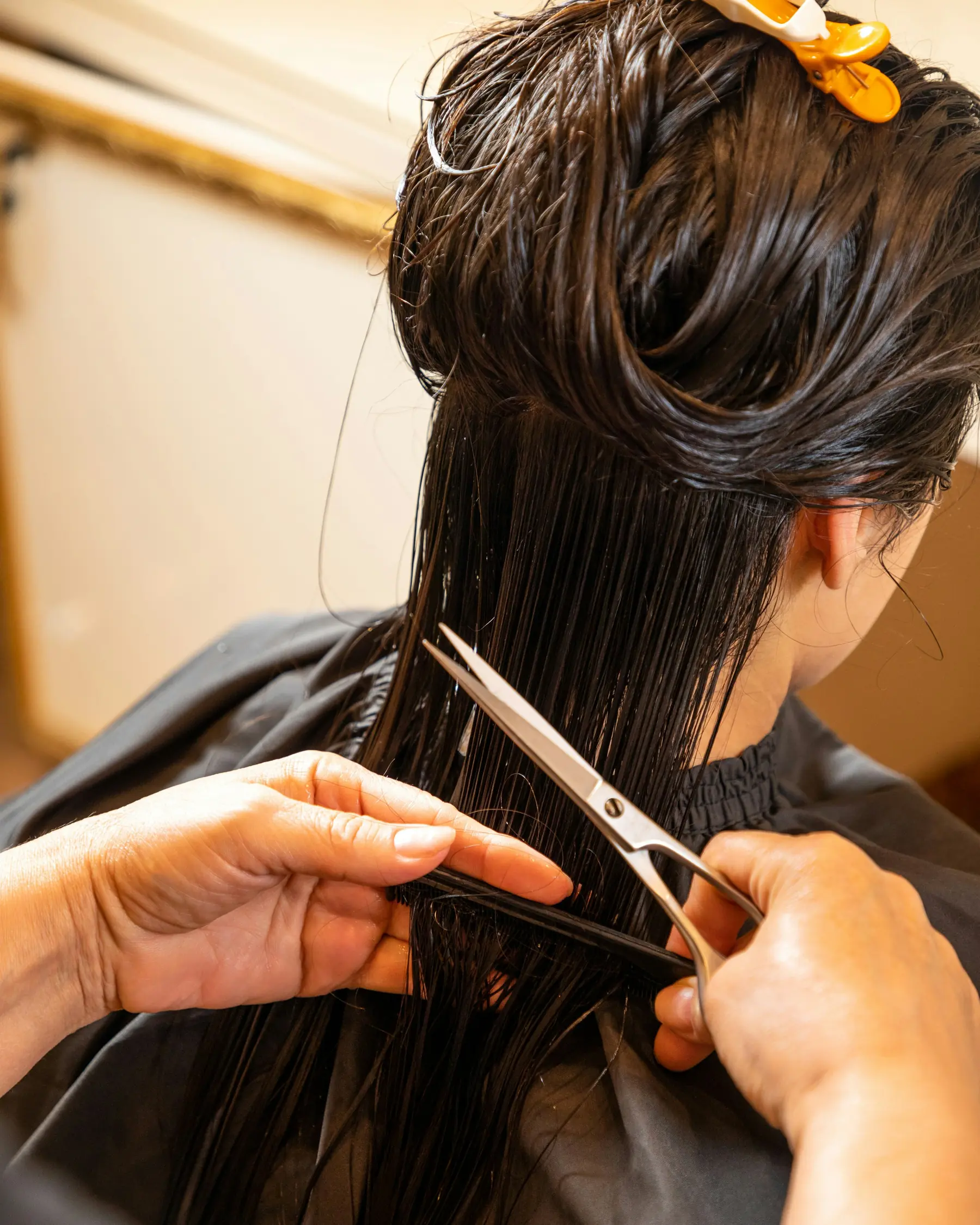 Stylist's hands trimming freshly washed hair with shears at the chair