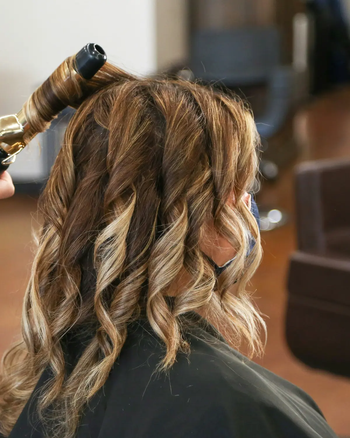 A stylist curling a client's hair at the styling chair
