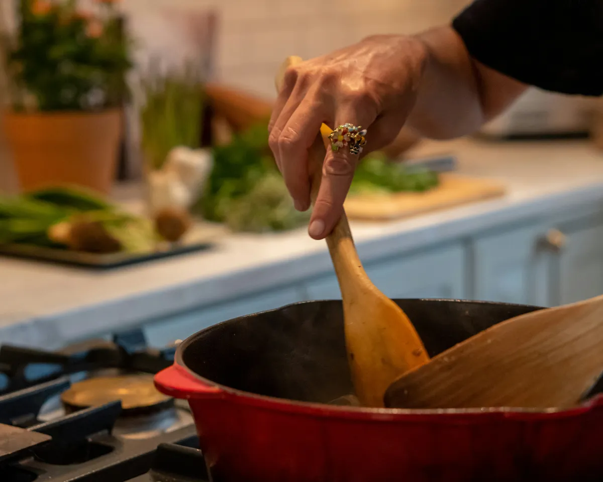 A hand stirring a pot of preserves on the stove with a wooden spoon