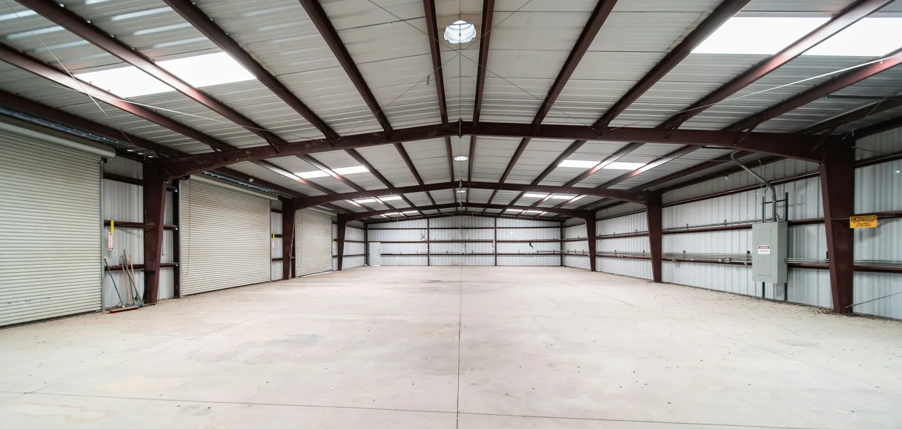 Empty industrial warehouse interior with exposed steel trusses and skylights over a clean concrete floor
